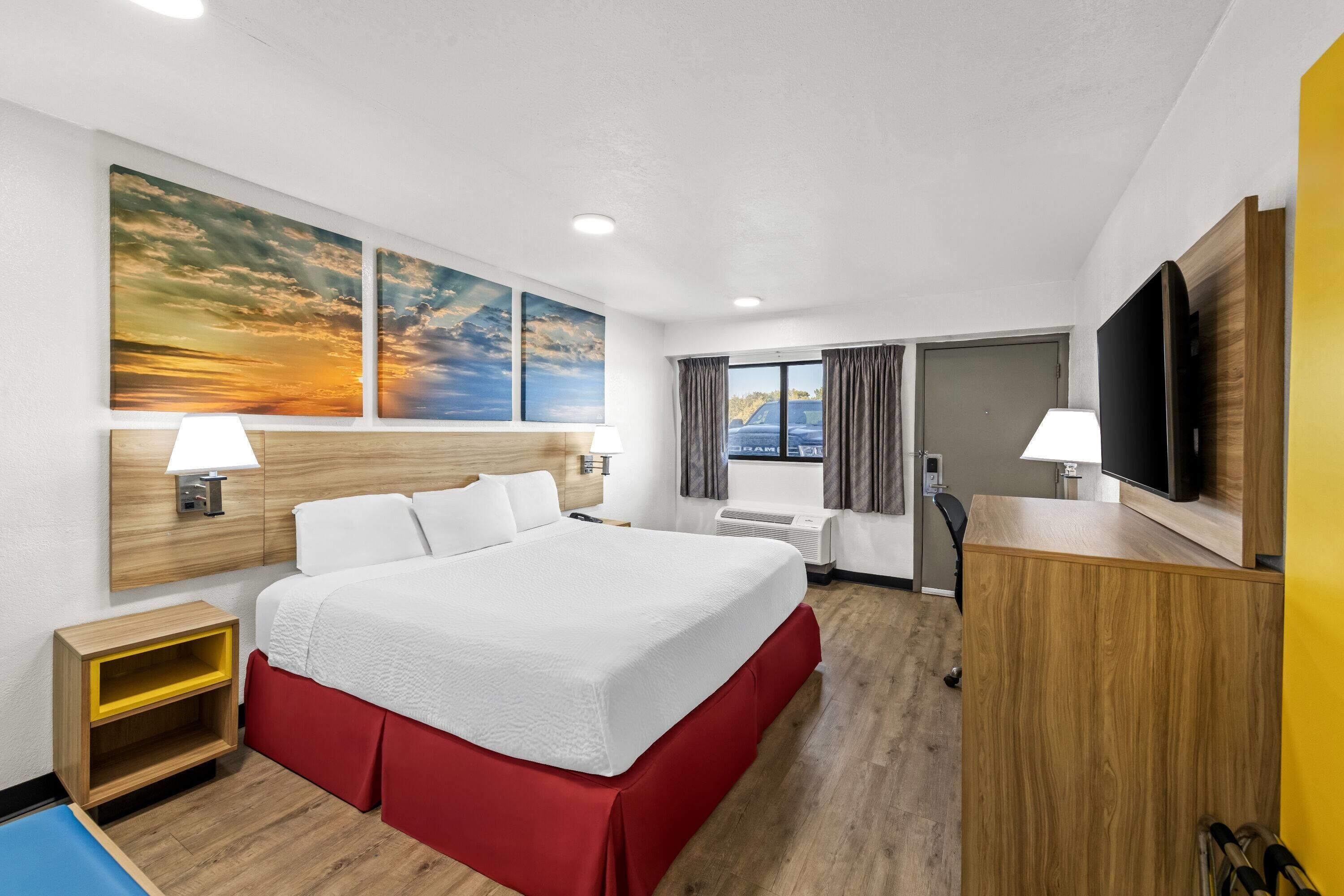 Habitación de hotel con una cama grande, dos lámparas fijadas a la pared, un televisor de pantalla plana y un ventanal con cortinas.