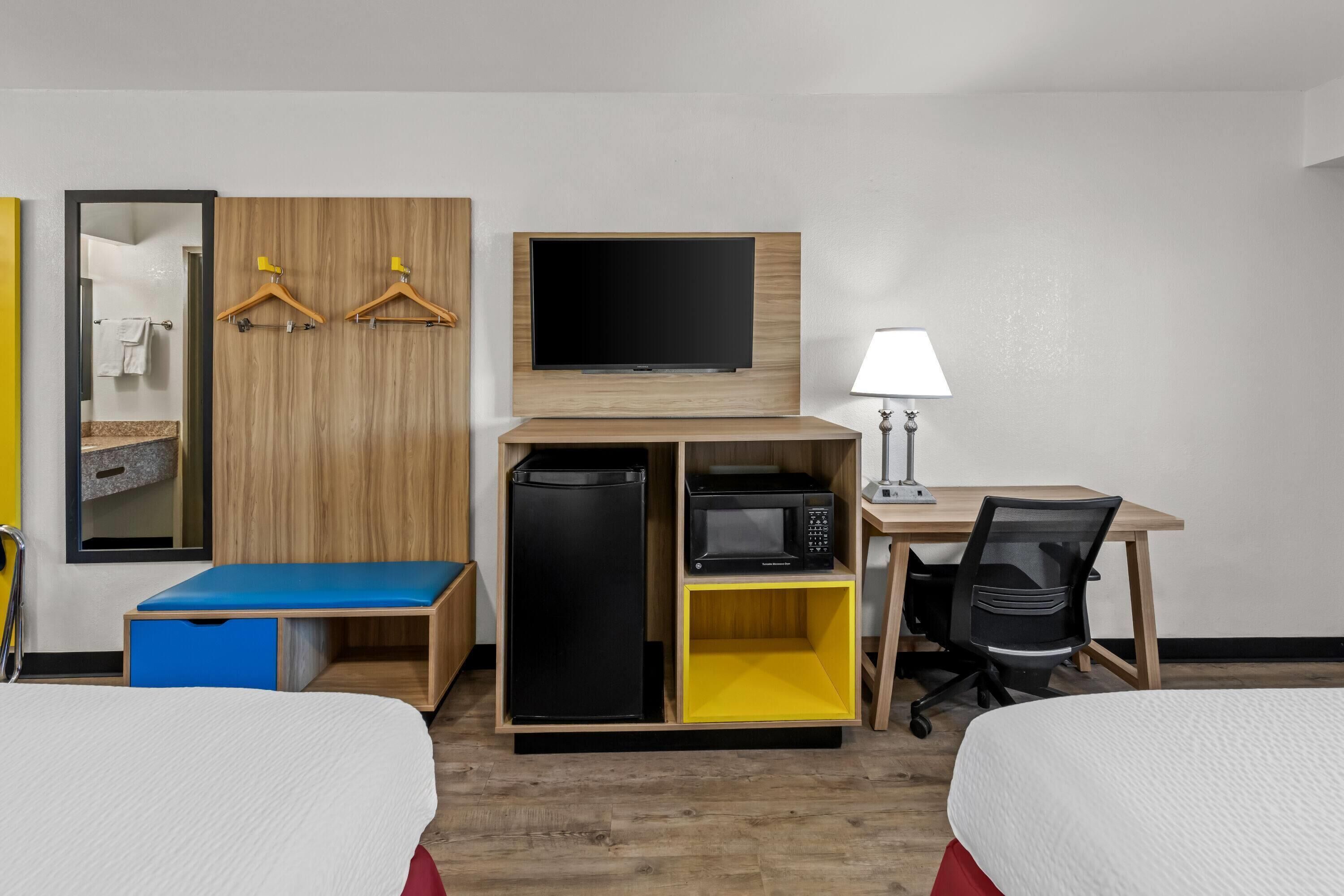 Habitación de hotel con dos camas, televisión, escritorio con lámpara, microondas y refrigerador pequeño.