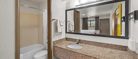 Un baño con bañera, inodoro, lavabo y un espejo grande.