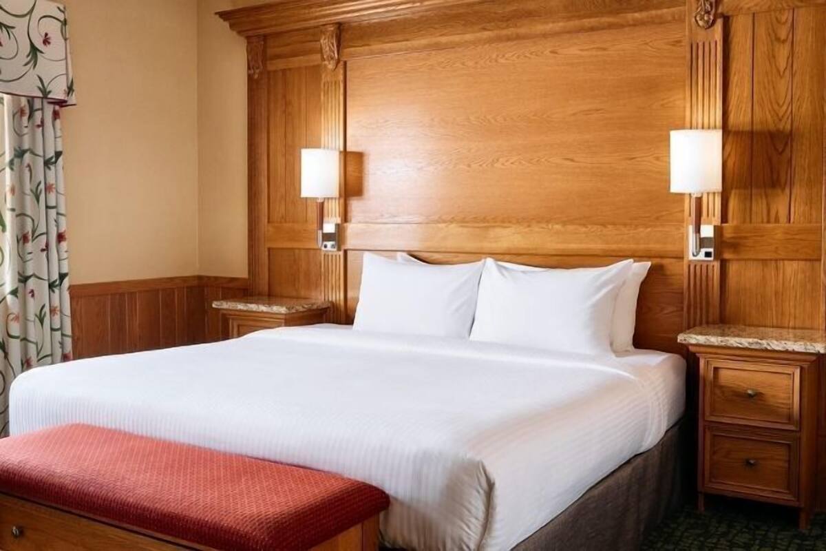 Une chambre d’hôtel avec un grand lit, une tête de lit en bois, des lampes de chevet et une fenêtre avec des rideaux.