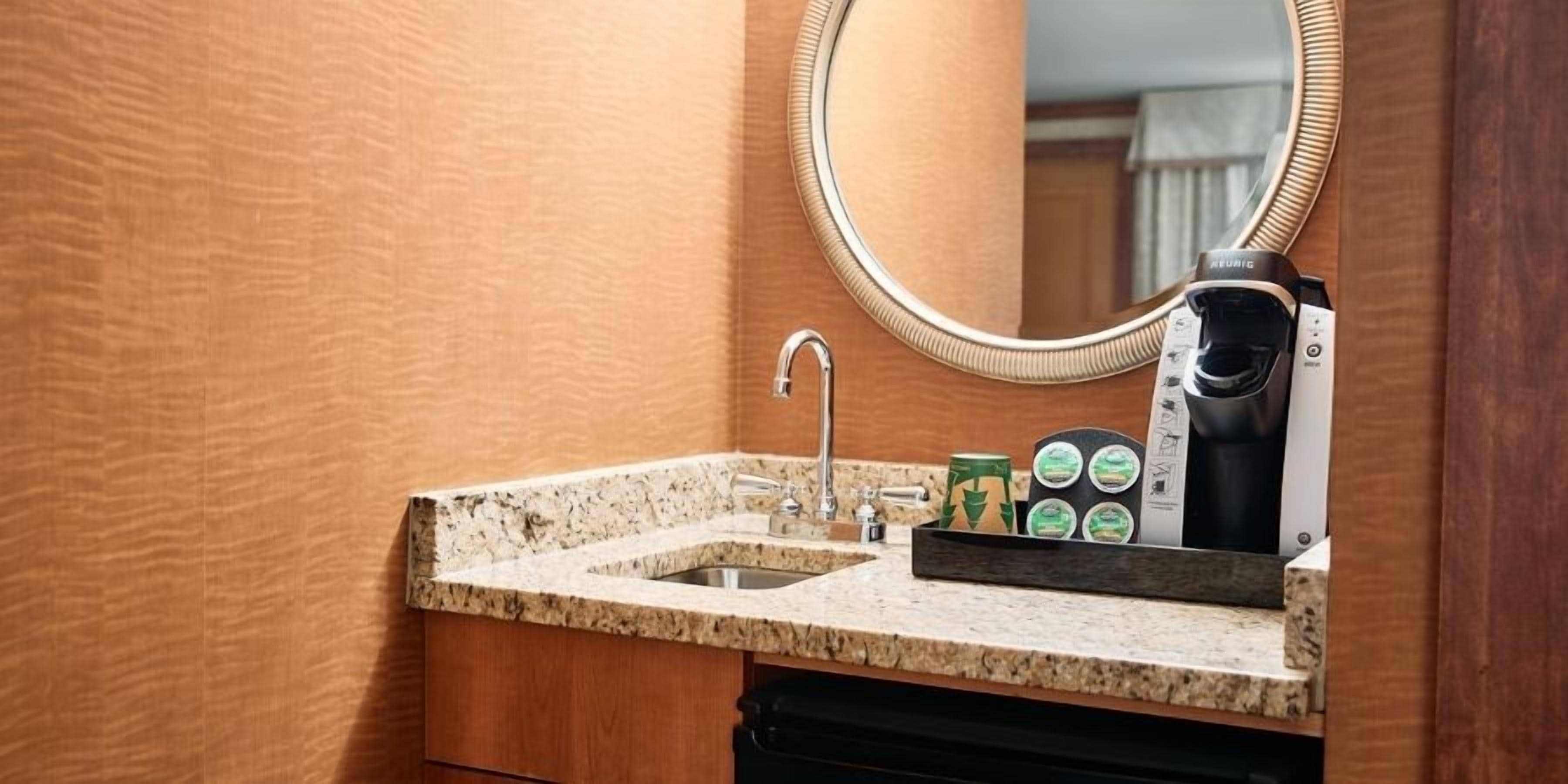 Baño con encimera de granito, lavamanos, espejo y cafetera.