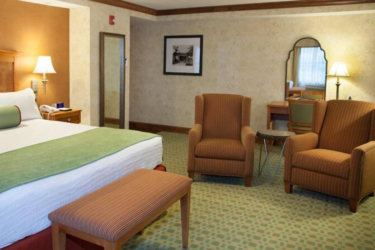 A hotel room with a large bed, two armchairs, a small table, and a bench.
