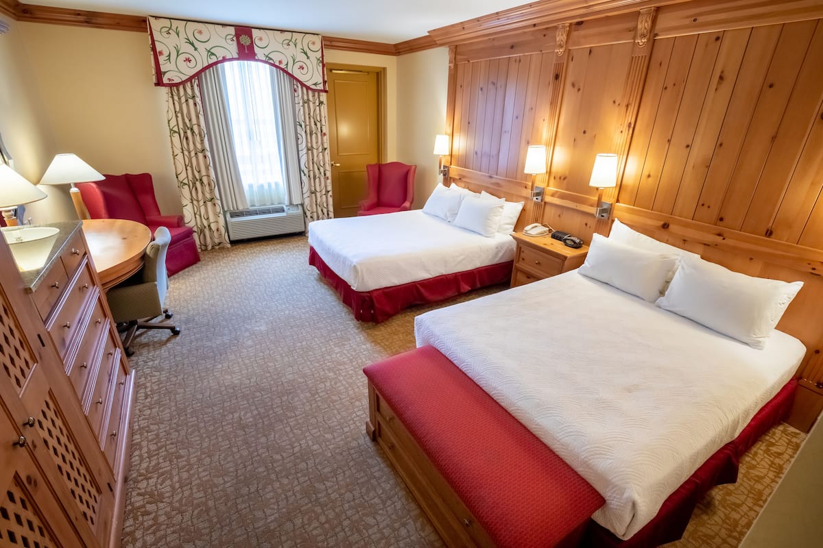 A hotel room with two beds, a desk, a chair, and a wardrobe.