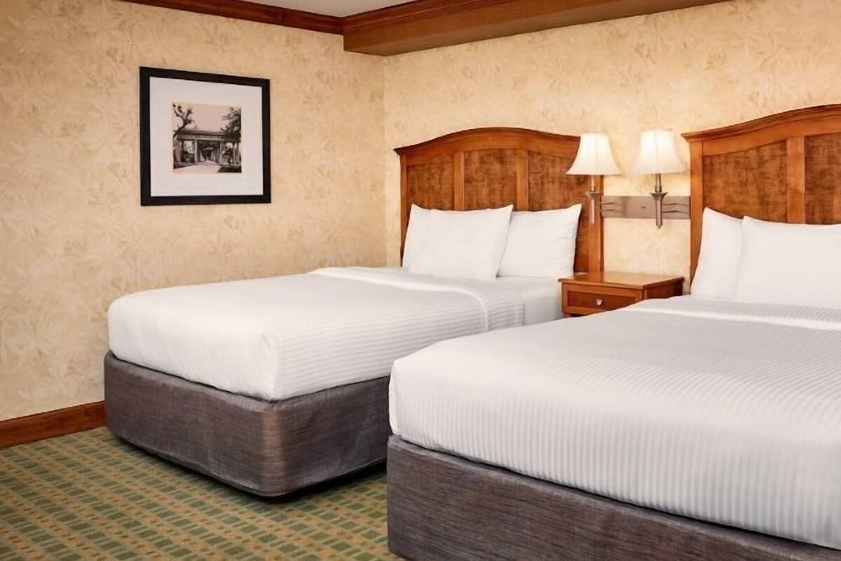 A hotel room with two beds, a framed picture on the wall, and a nightstand with lamps.