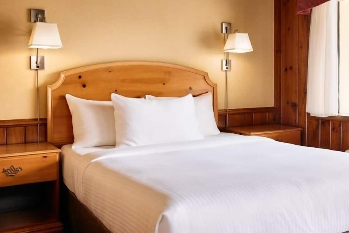 A neatly made bed with white linens in a room with wooden paneling and two bedside lamps.