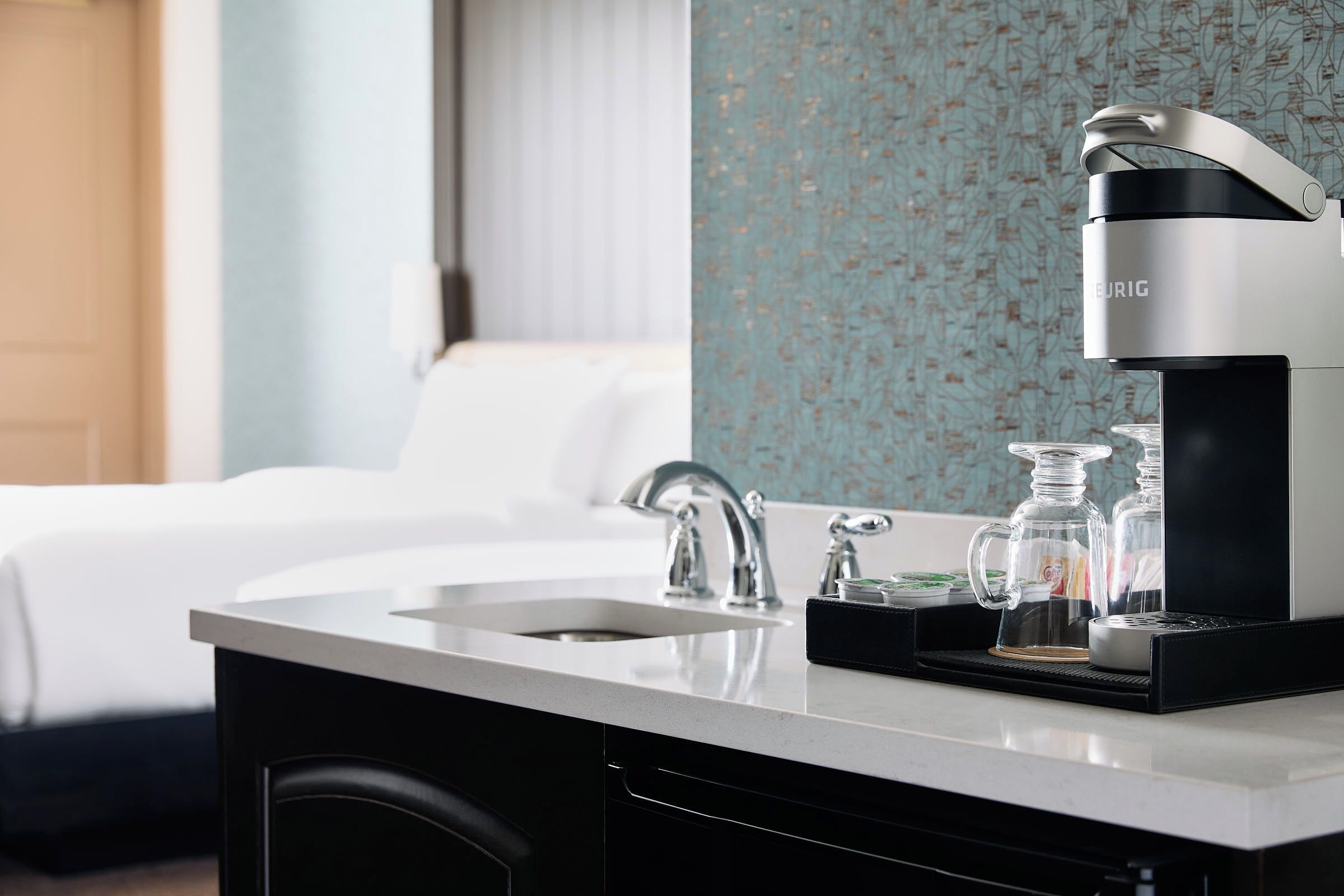 A modern hotel room with a kitchen area including a coffee maker, sink, and countertop.