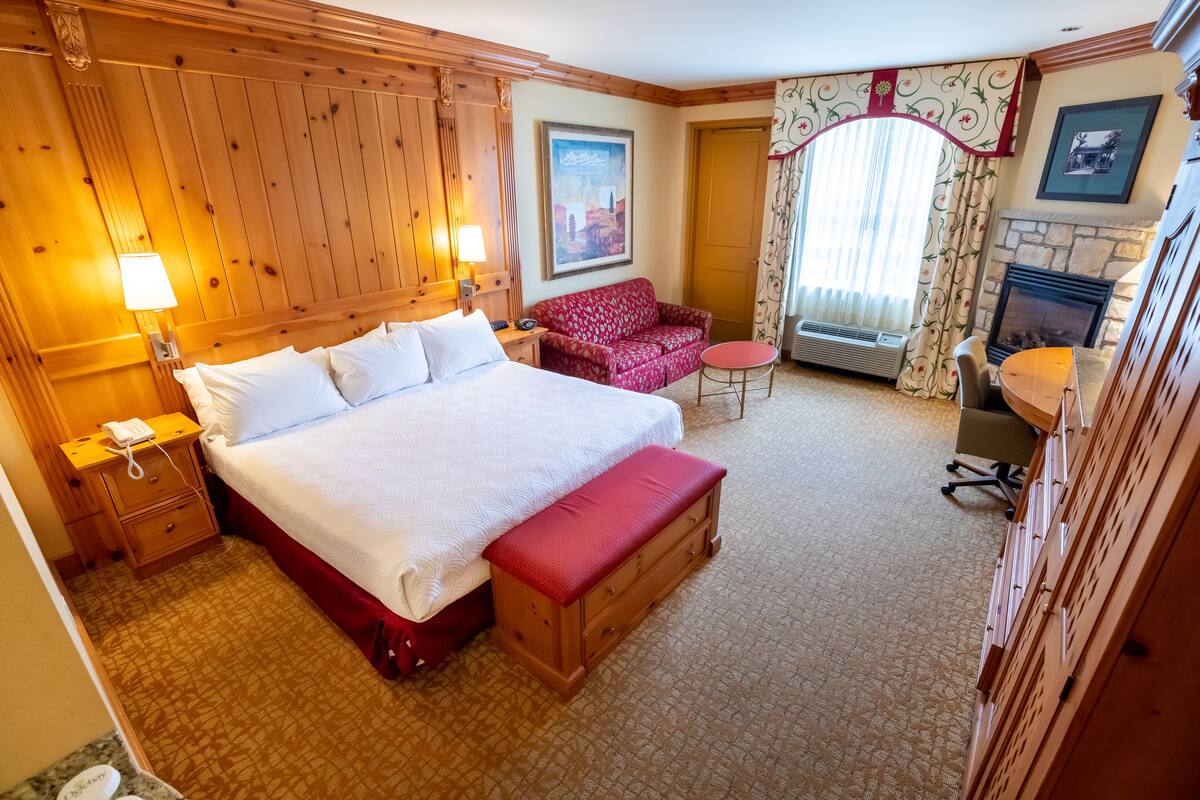 A hotel room with a large bed, a red sofa, a small table, and a fireplace.