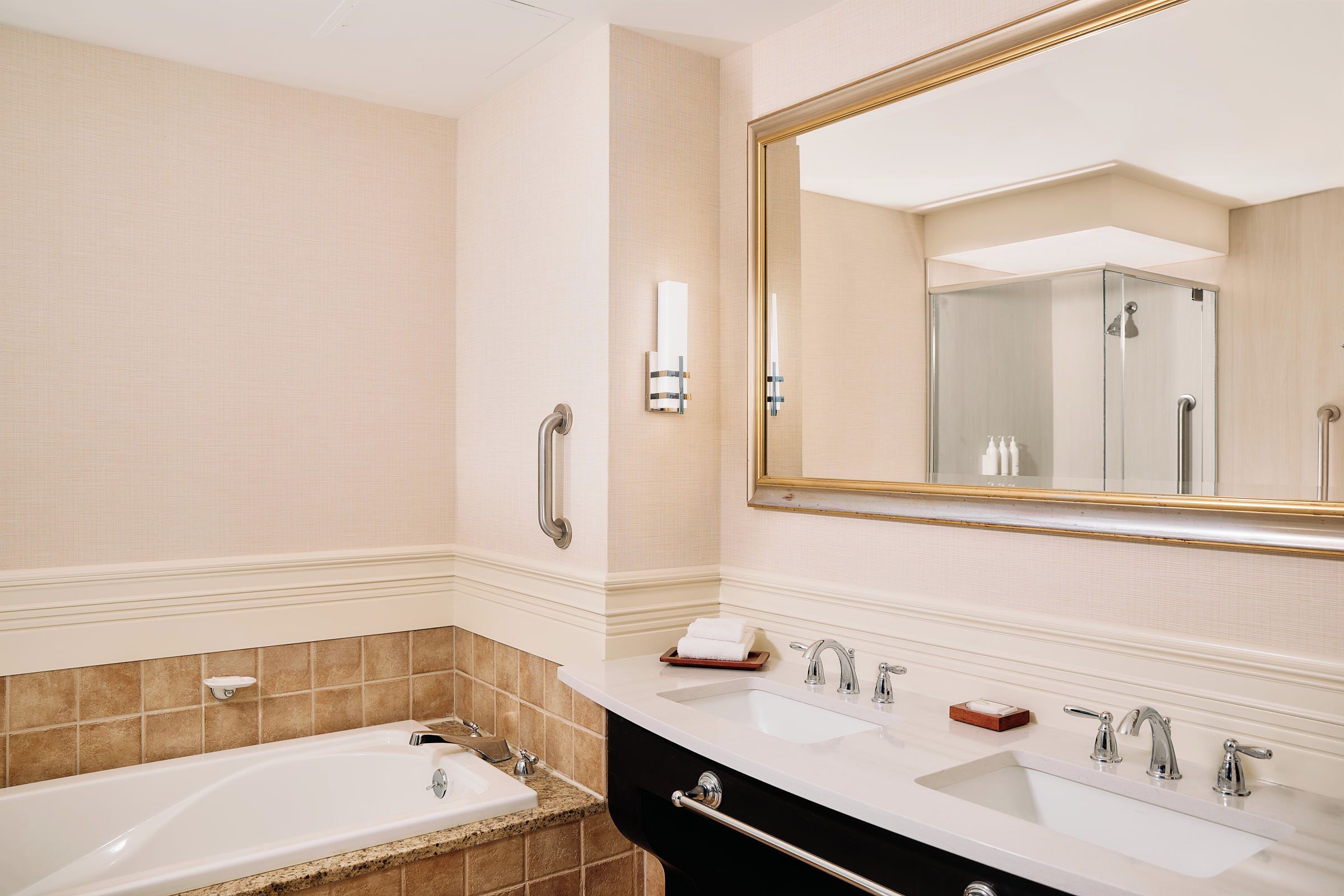 A bathroom with a bathtub, two sinks, a large mirror, and a towel rack.