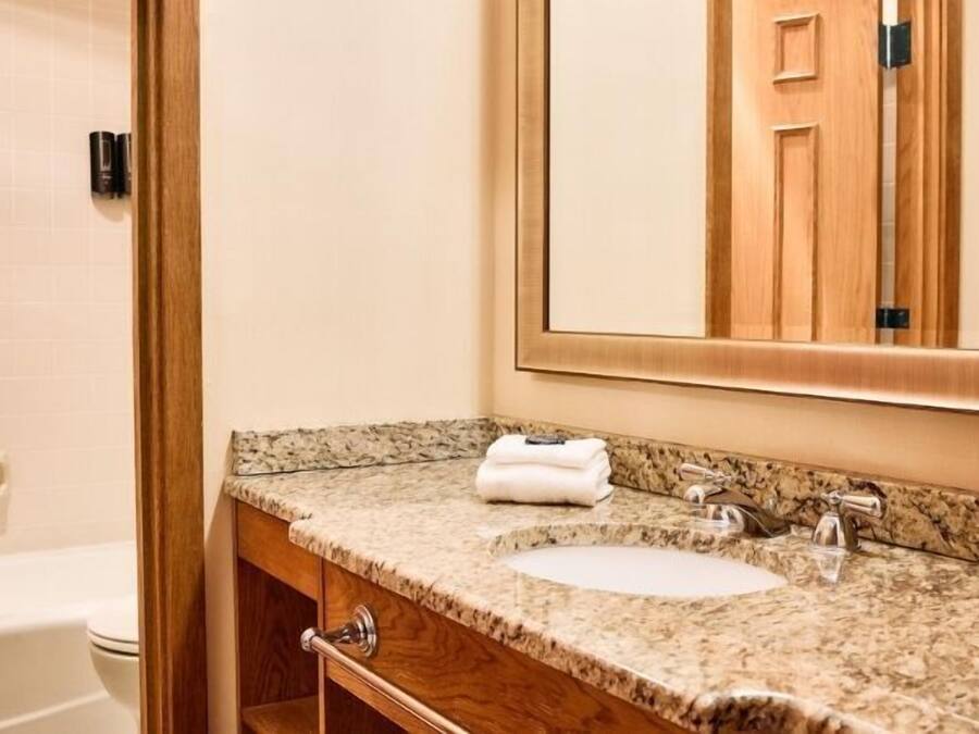 Une salle de bain avec un comptoir en granit, un lavabo, un miroir et un meuble-lavabo en bois.