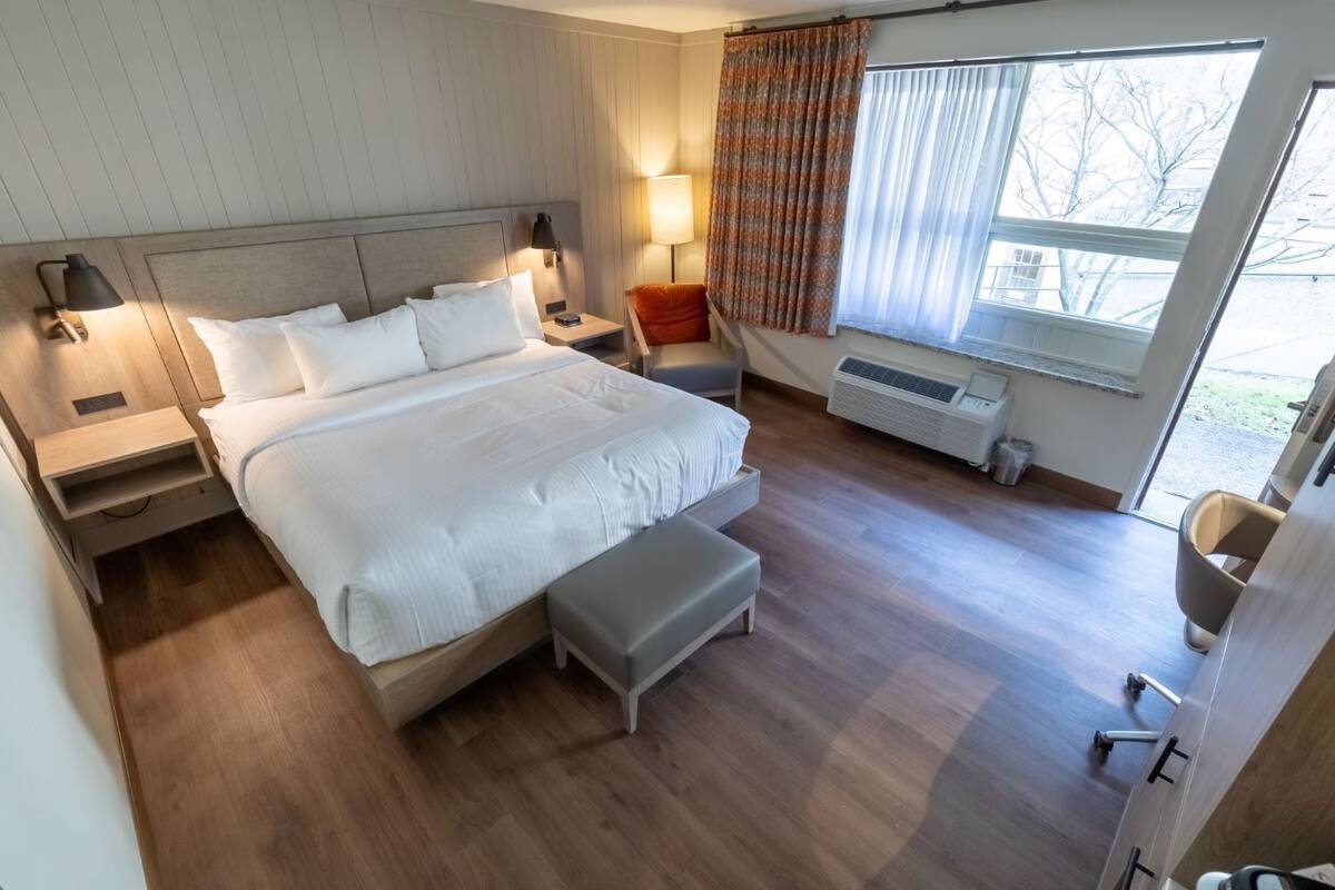 Une chambre d’hôtel moderne avec un grand lit, des tables de chevet, un bureau et une fenêtre avec des rideaux.