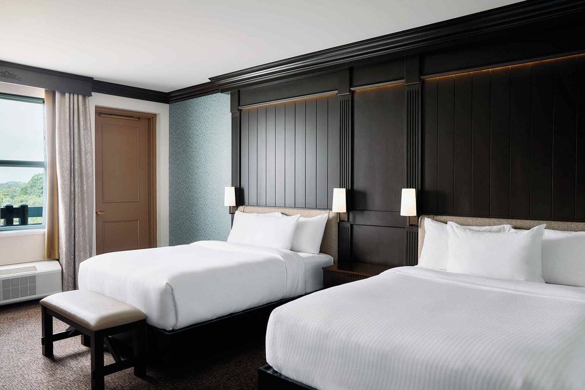 Une chambre d’hôtel avec deux lits, un banc, une fenêtre avec des rideaux et une vue sur la verdure.