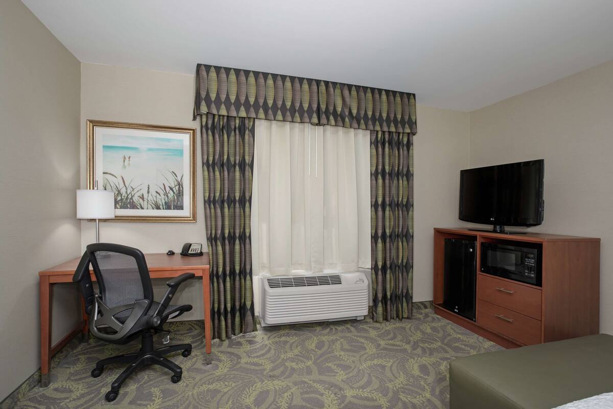 Une chambre d’hôtel équipée d’un bureau, d’une chaise, d’une télévision, d’un système de climatisation et d’un lit.