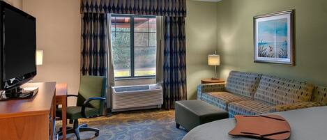 A hotel room with a bed, a sofa, a desk with a TV, an air conditioning unit, and a window with curtains.