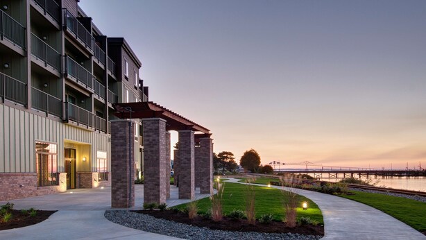 A modern building with a covered walkway, a river view, and a bridge in the background. - Hampton Inn and Suites Astoria (Astoria)