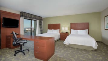 A hotel room with a desk, two beds, a TV, and a view of the outside.