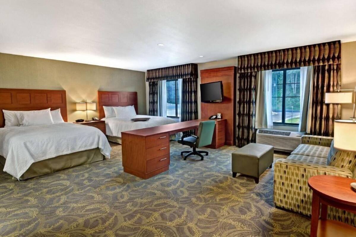 Une chambre d’hôtel avec deux lits, un bureau, une chaise, un canapé et une télévision.