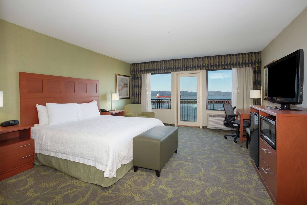 Une chambre d’hôtel avec un grand lit, un bureau avec un ordinateur, une télévision et une vue sur l’eau.
