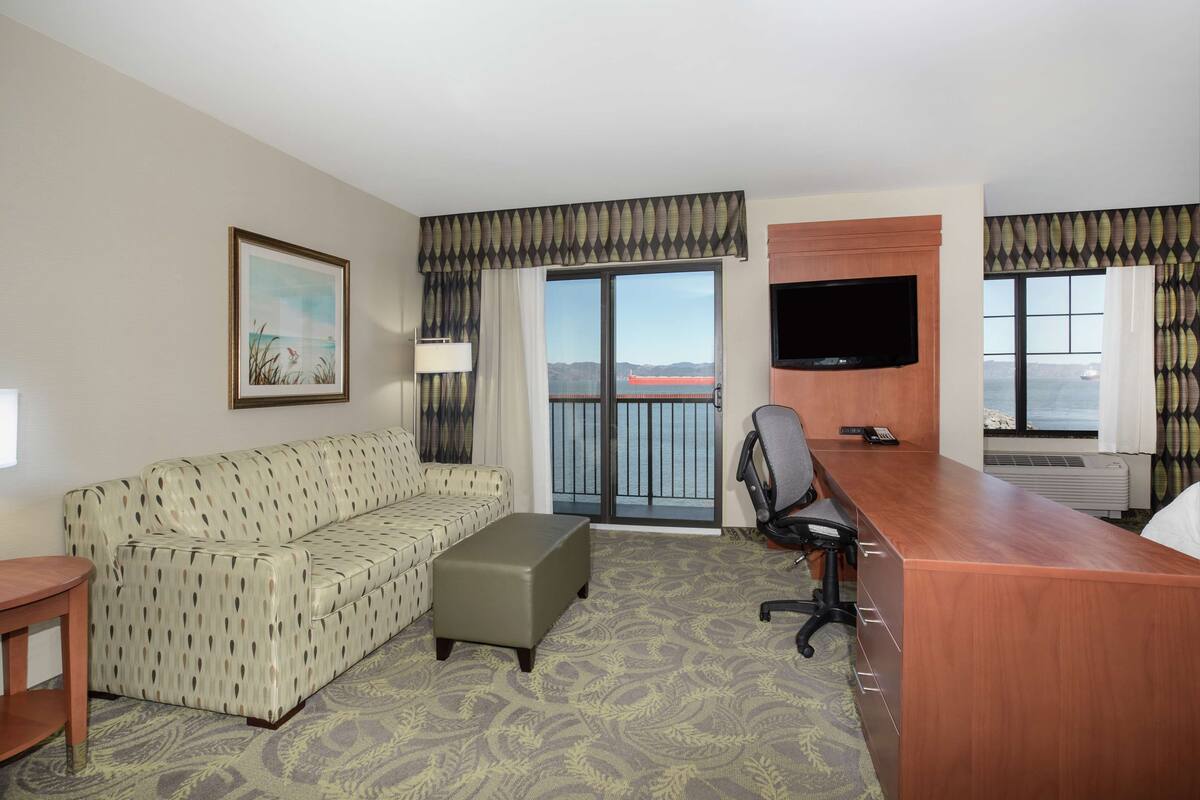 Une chambre d’hôtel avec un canapé, un bureau, une télévision et un balcon offrant une vue.