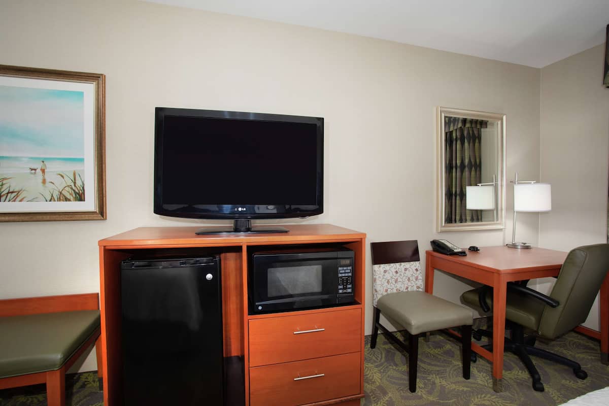 Une chambre d’hôtel équipée d’une télévision, d’un réfrigérateur, d’un four à micro-ondes, d’un bureau, d’une chaise et d’un petit banc.