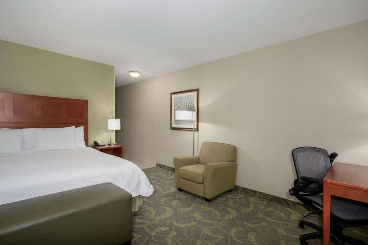 Une chambre d’hôtel avec un lit, un bureau, une chaise, une lampe et un tableau encadré au mur.