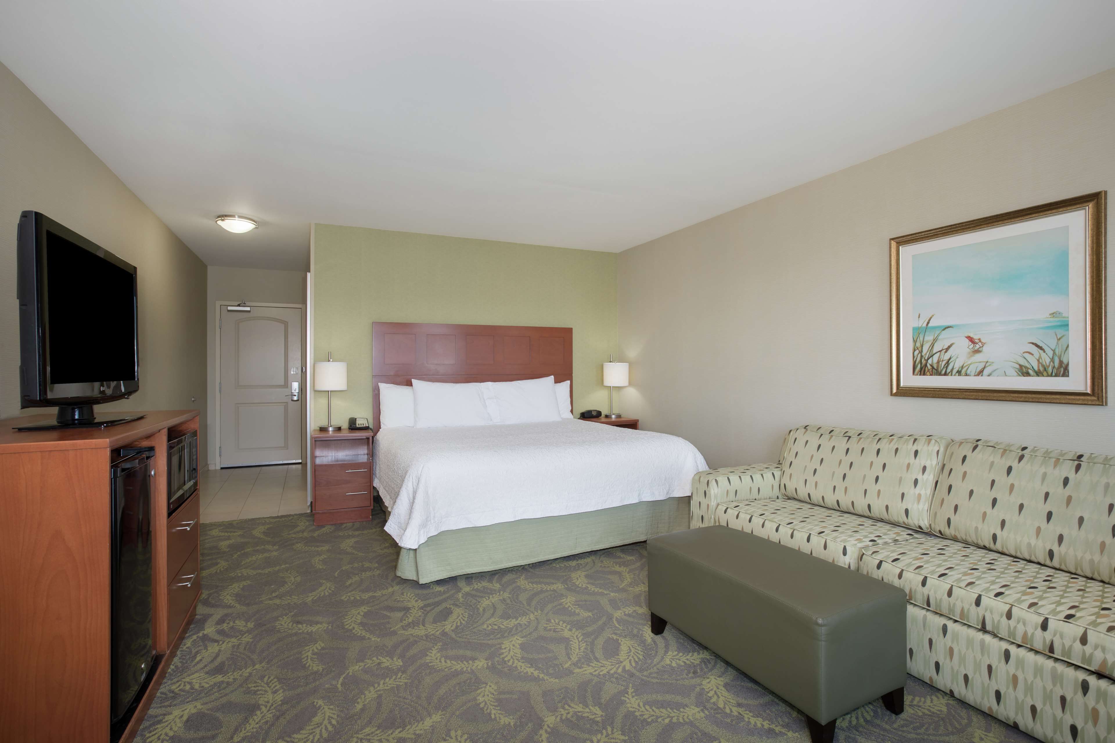 Quarto de hotel com cama, televisão, sofá e um quadro na parede.