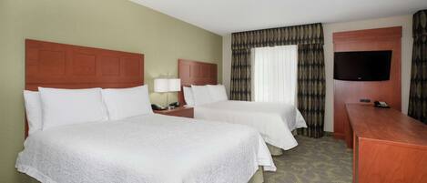 A hotel room with two beds, a TV, a desk, and a window with curtains.