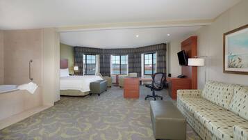 A hotel room with a bed, a desk, a chair, a sofa, a bathroom, and a large window offering a view.