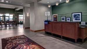 A hotel reception area with a wooden desk, a reception counter, a patterned rug, and framed pictures on the wall. - Hampton Inn and Suites Astoria (Astoria)