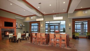 A spacious living area with a fireplace, a large dining table with chairs, and a view of the outdoors through large windows. - Hampton Inn and Suites Astoria (Astoria)
