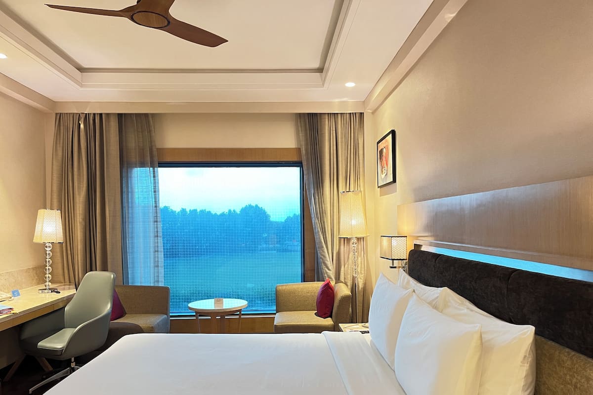 Habitación de hotel con una cama grande, un escritorio con una silla, una mesita y vistas al exterior.