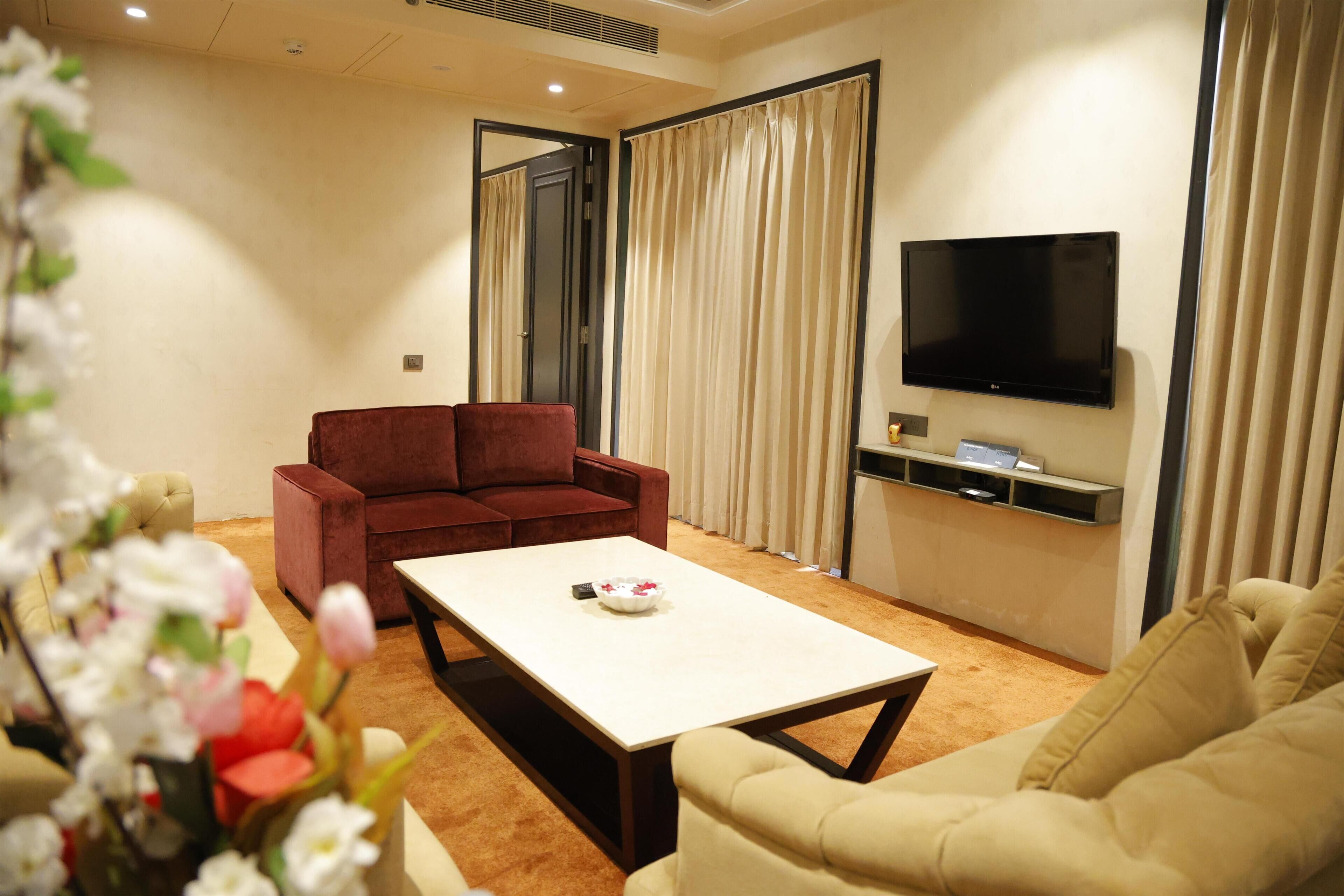 A modern living room with a beige sofa, a red sofa, a coffee table, and a flat-screen TV mounted on the wall.