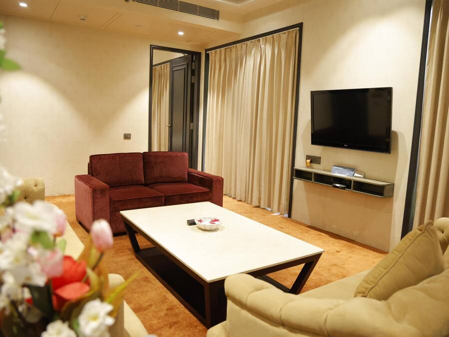 A modern living room with a beige sofa, a red sofa, a coffee table, and a flat-screen TV mounted on the wall.