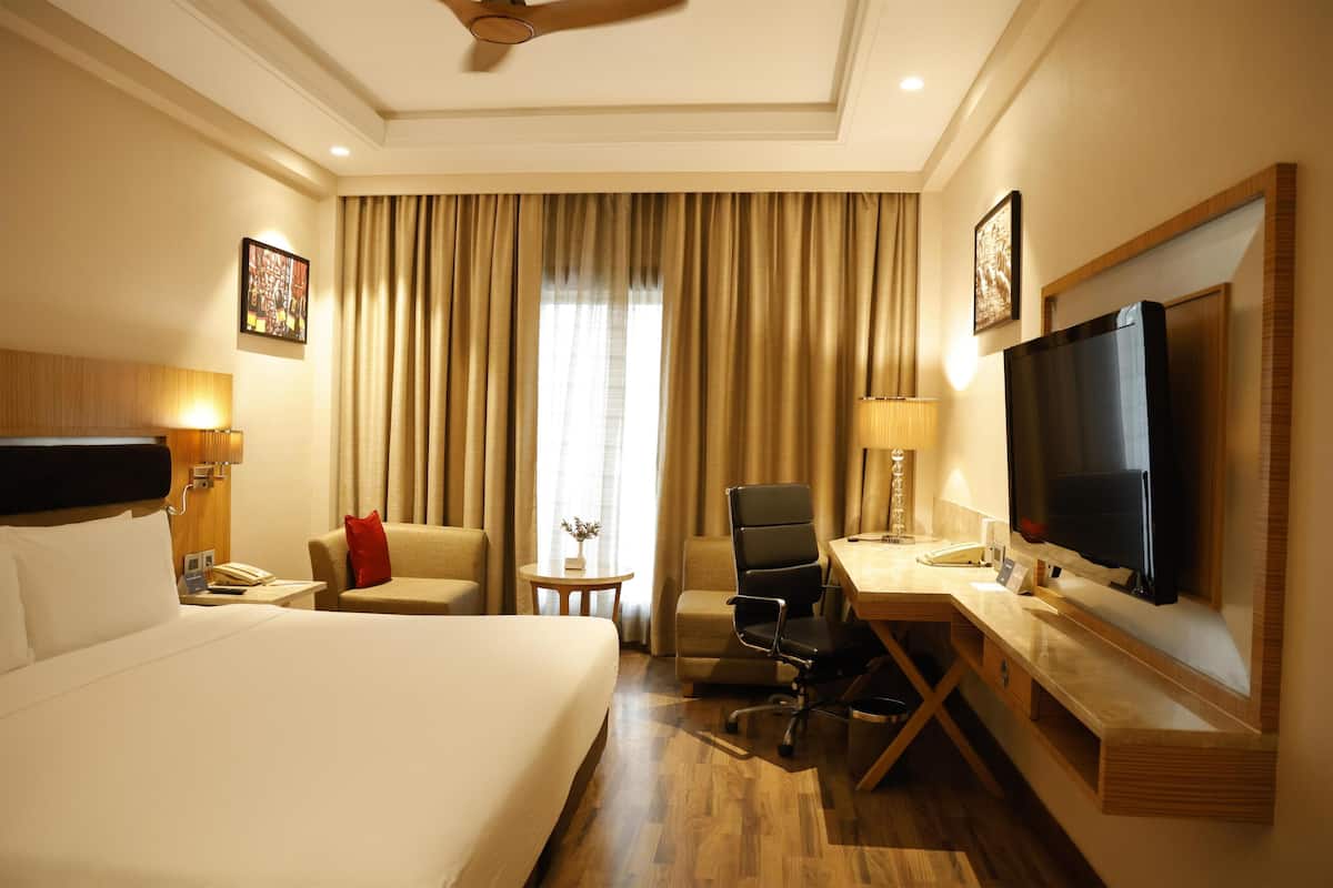Habitación de hotel con una cama grande, un escritorio con silla, televisor y ventana con cortinas.