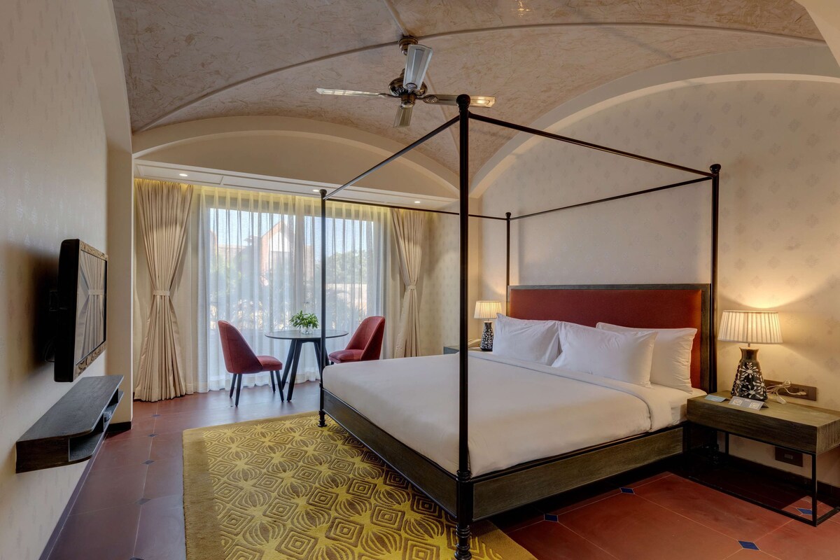 Un letto a baldacchino con testiera rossa, un comodino con una lampada e un tavolino con una pianta.