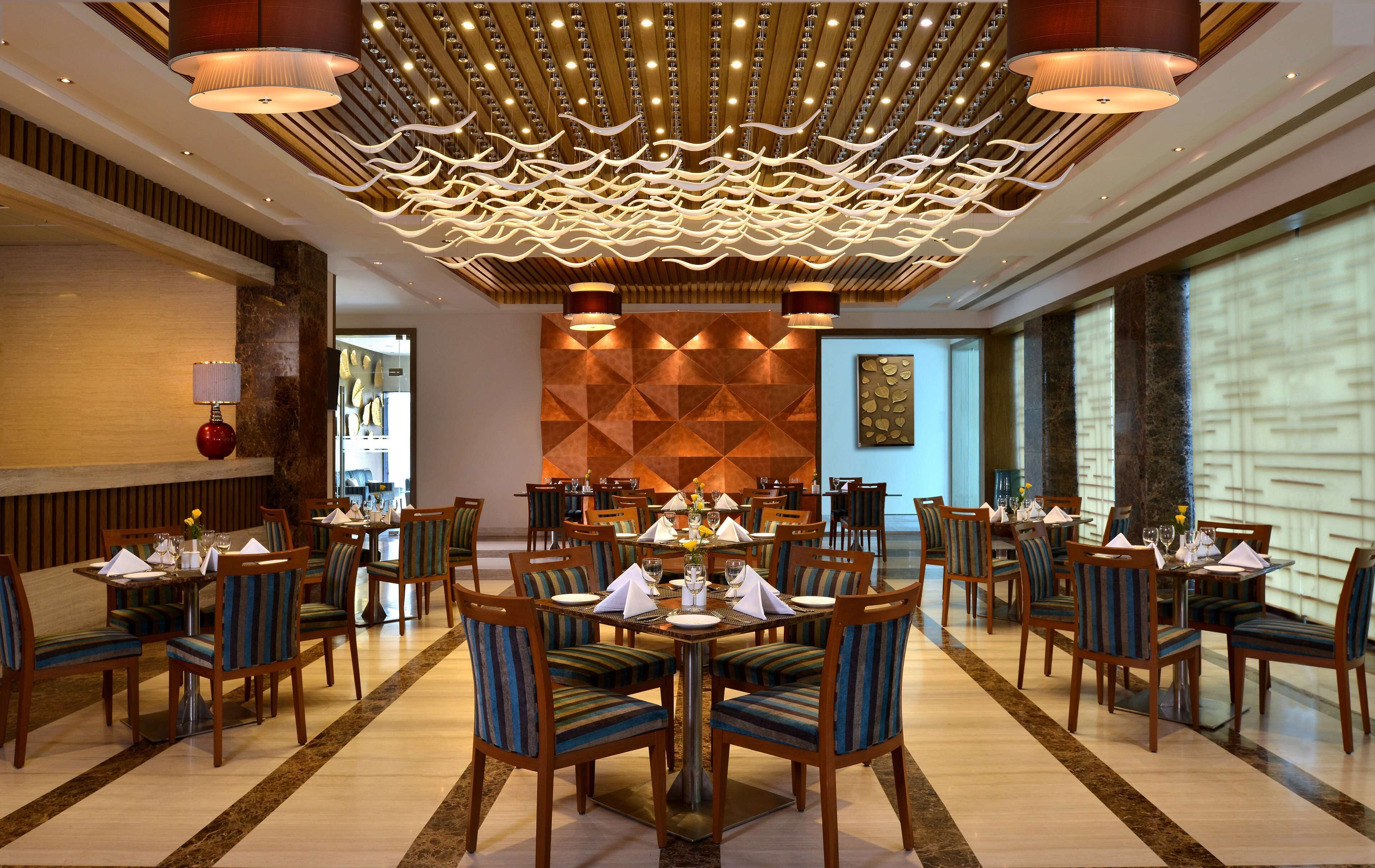 A spacious dining area with multiple tables and chairs, a decorative ceiling, and a patterned wall in the background.