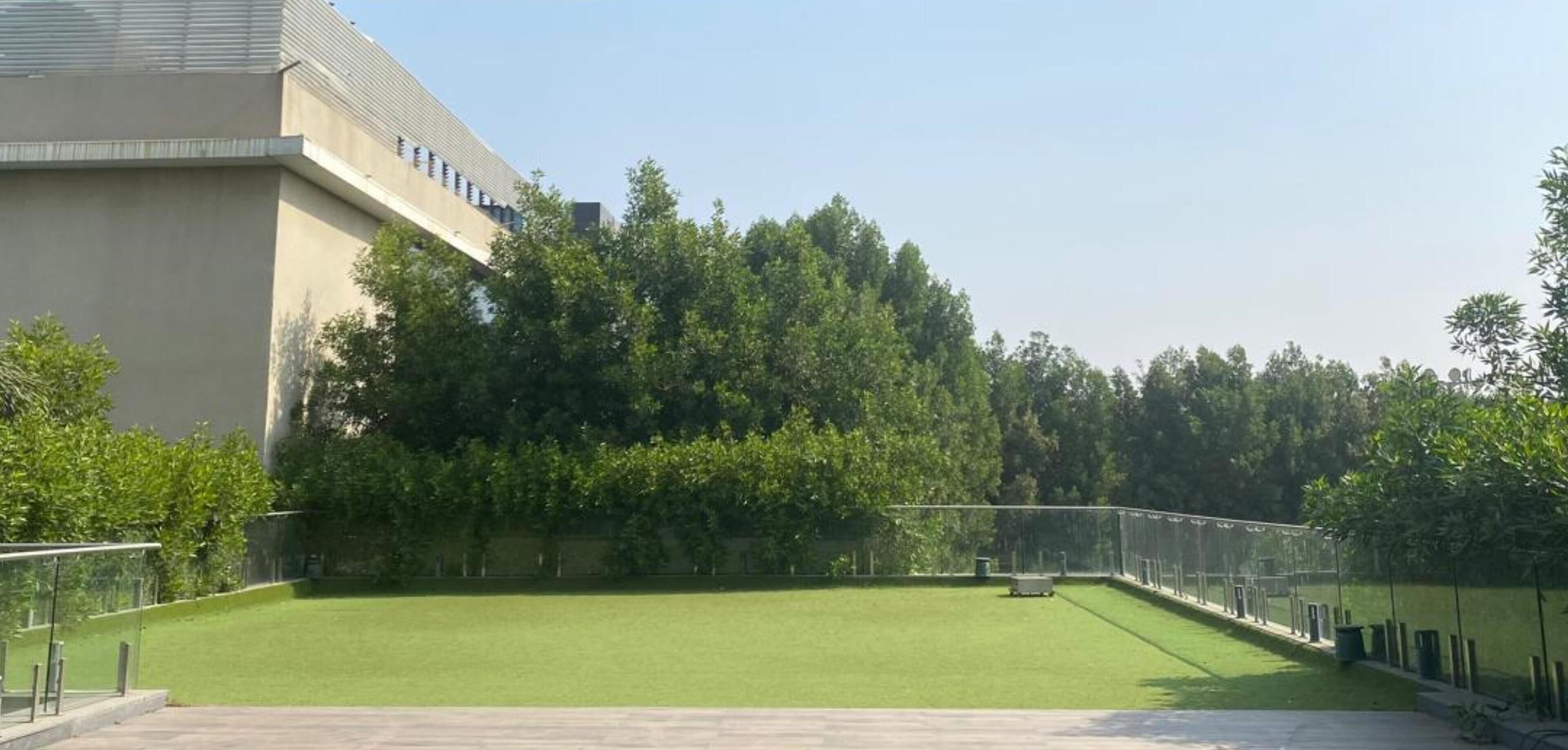 Un patio con césped verde, un edificio de diseño moderno y una cerca delimitando el espacio.