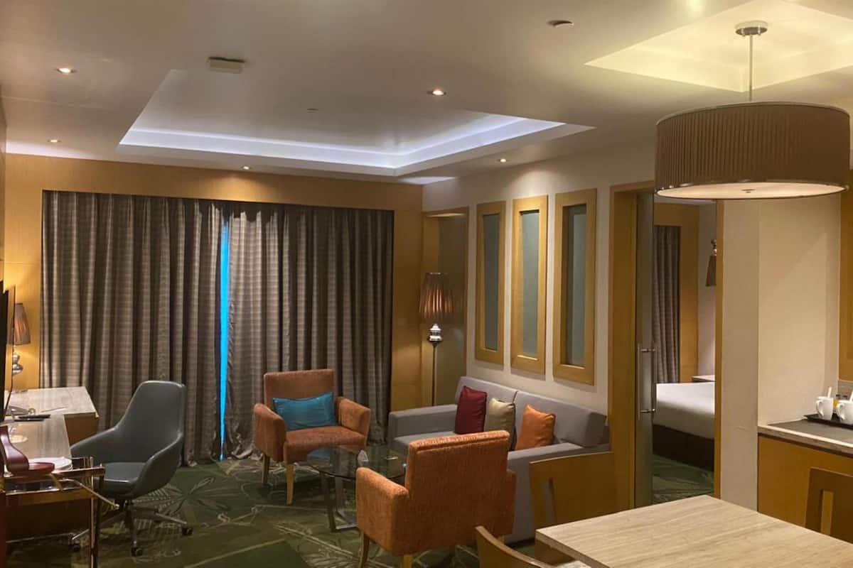 Habitación de hotel con escritorio, dos sillones, un sofá, una cama, un espejo grande y una zona de comedor.