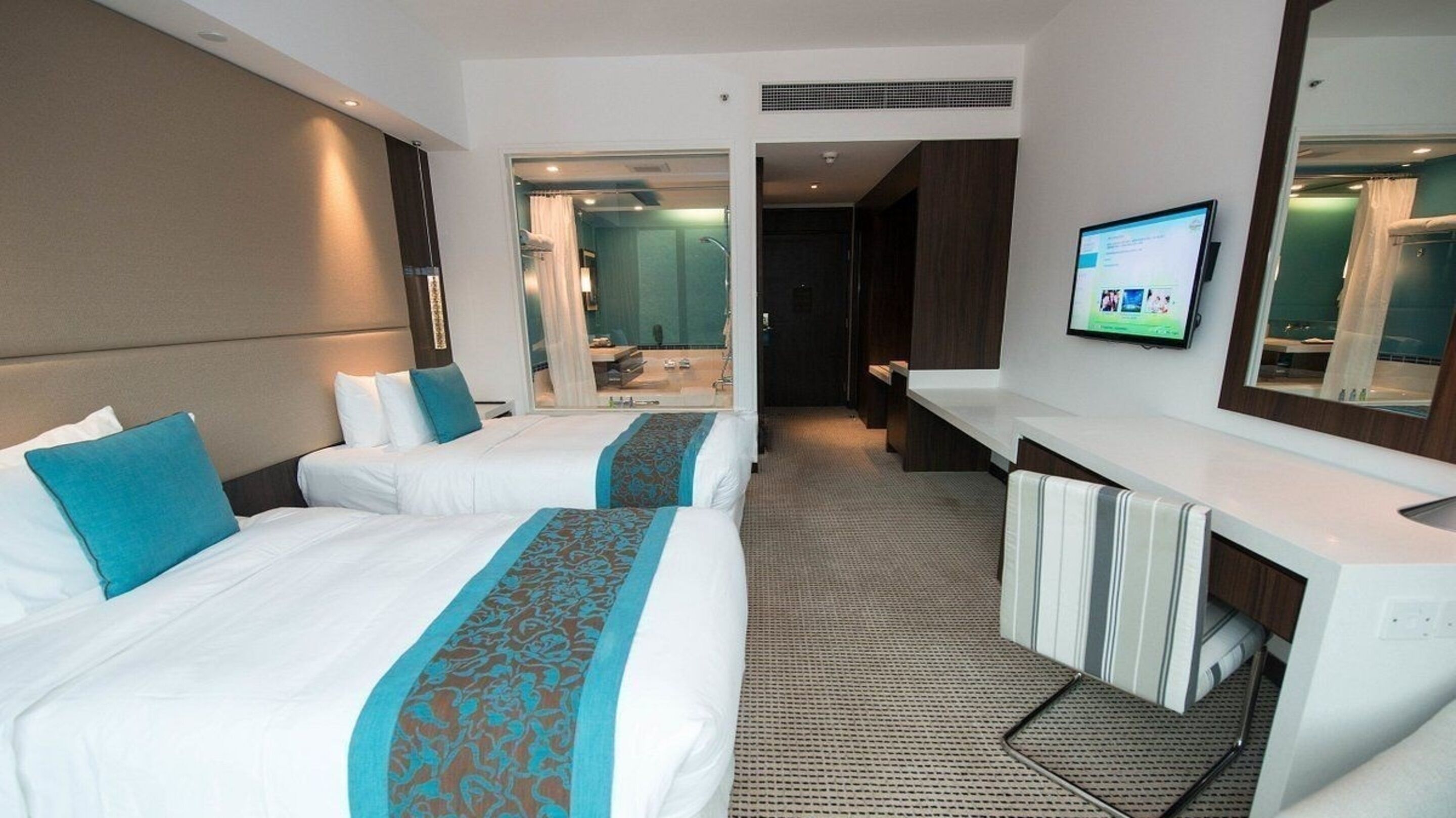Habitación de hotel con dos camas, baño, televisión y escritorio.