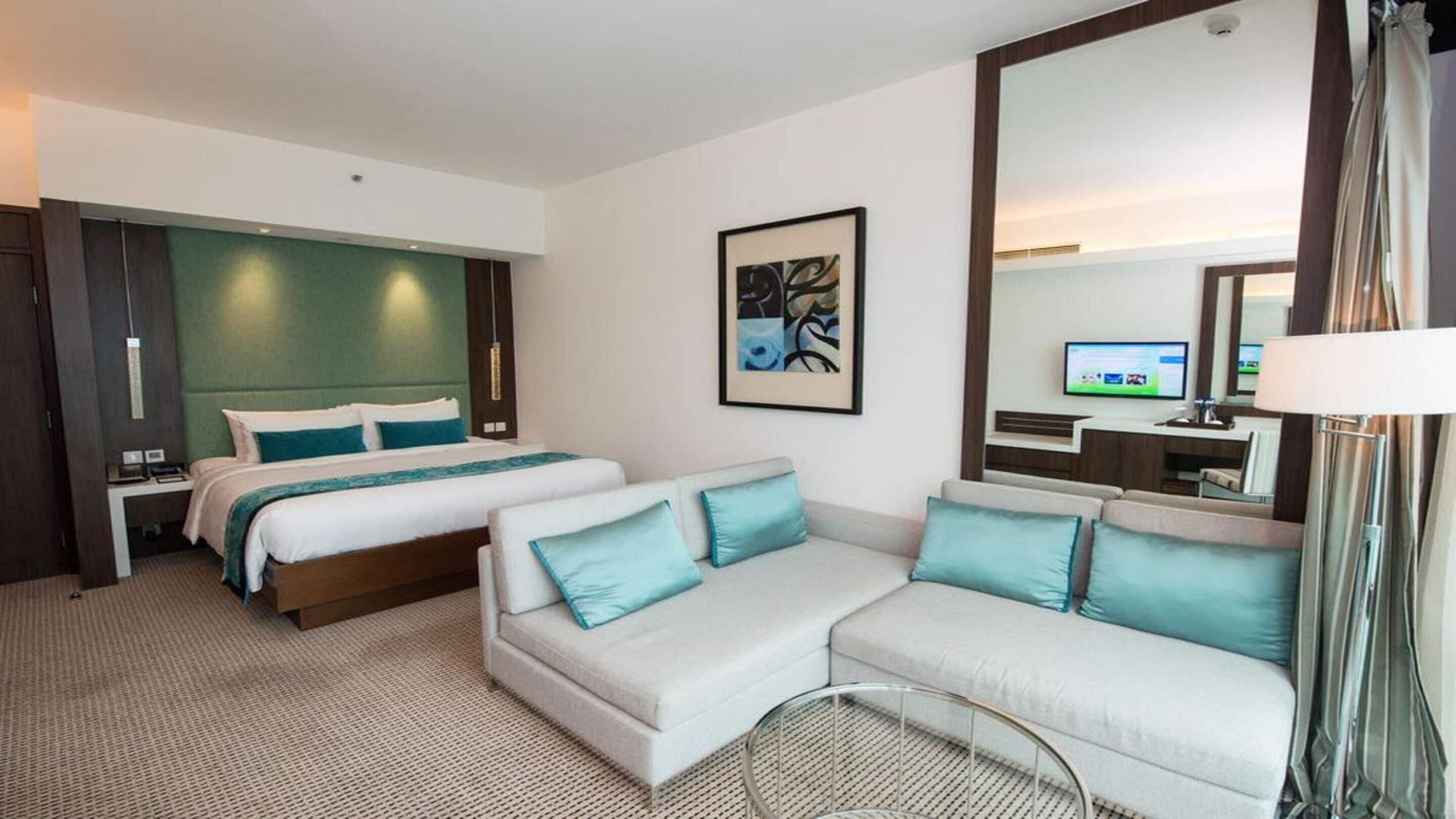 Habitació d'hotel amb un llit, un sofà, una televisió i un mirall gran.