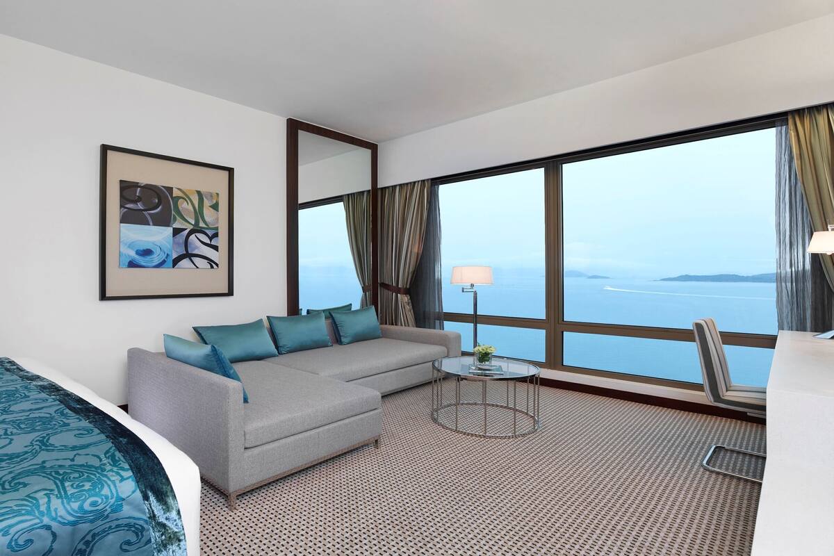 A modern hotel room with a large window, a sofa, a small table, and a bed.