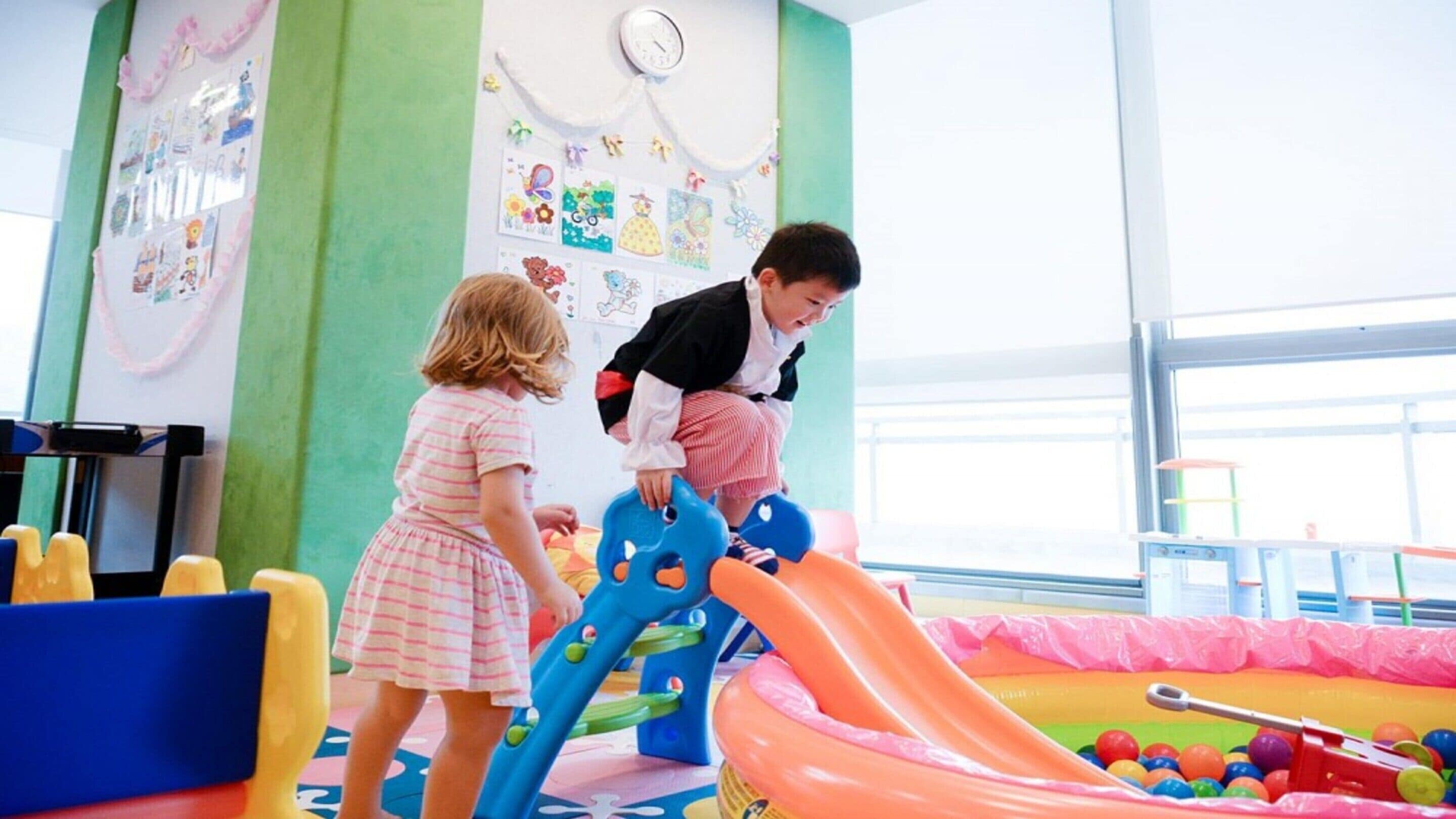 A children's play area with a slide and ball pit, featuring colorful decorations and a clock on the wall.