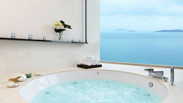 Een moderne badkamer met een groot bad, uitzicht op zee en een plank met toiletartikelen.
