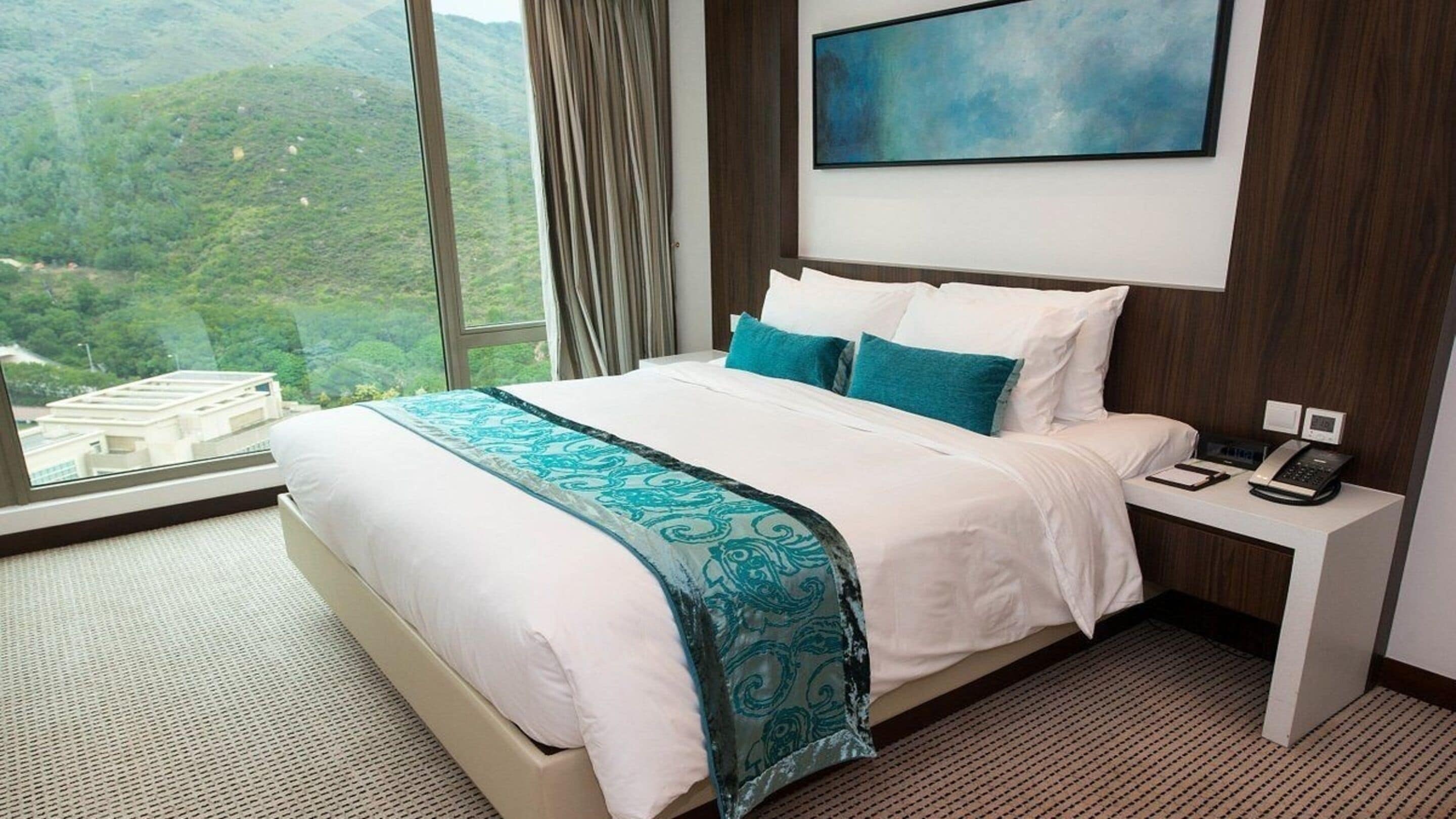 A hotel room with a large bed, a nightstand with a phone, and a painting on the wall.