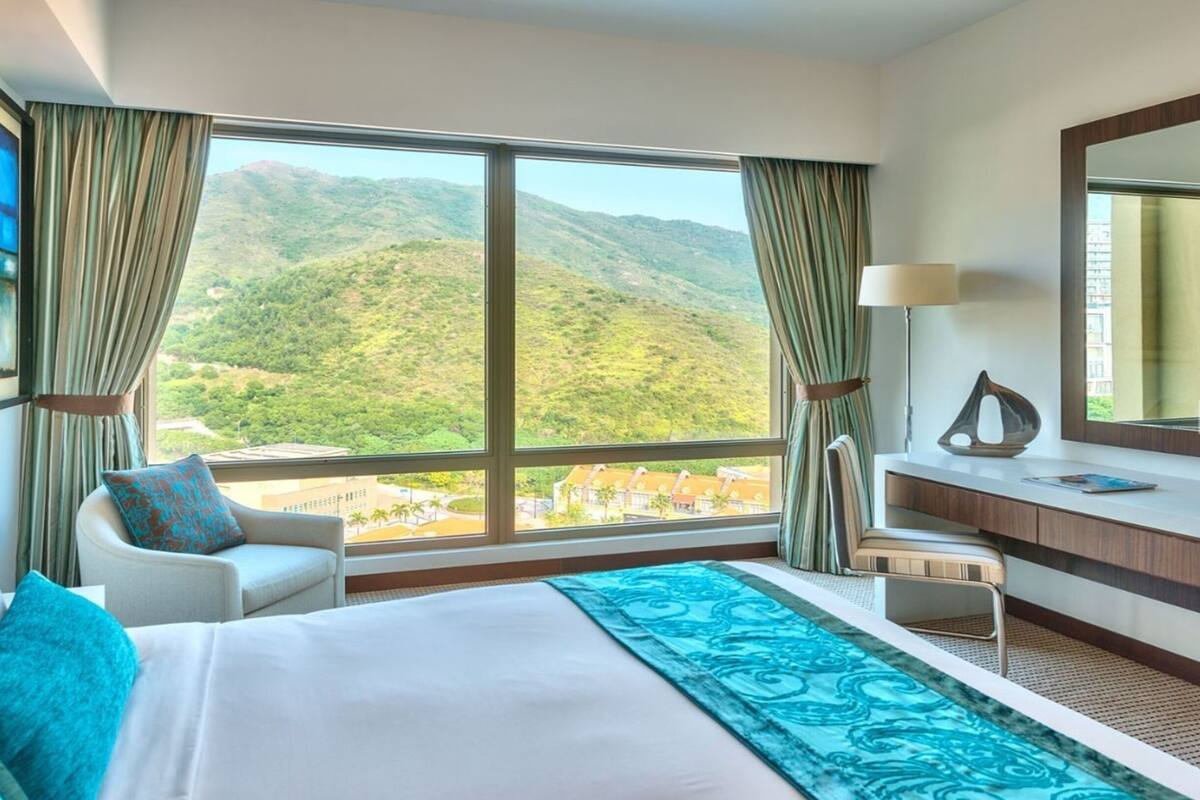 A hotel room with a large bed, a sitting area, a desk, and a view of a mountainous landscape.