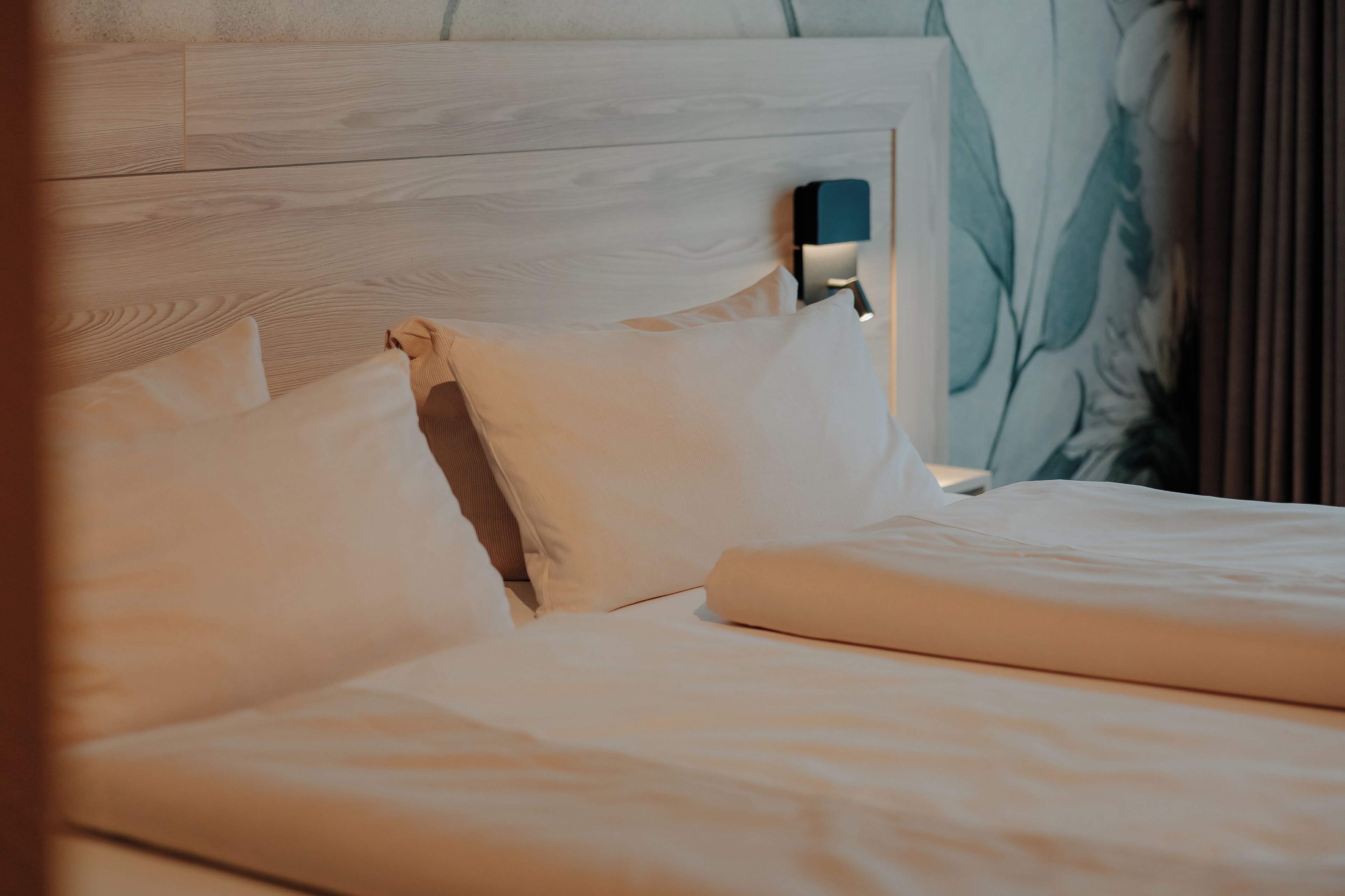 A neatly made bed with white linens and a wooden headboard.