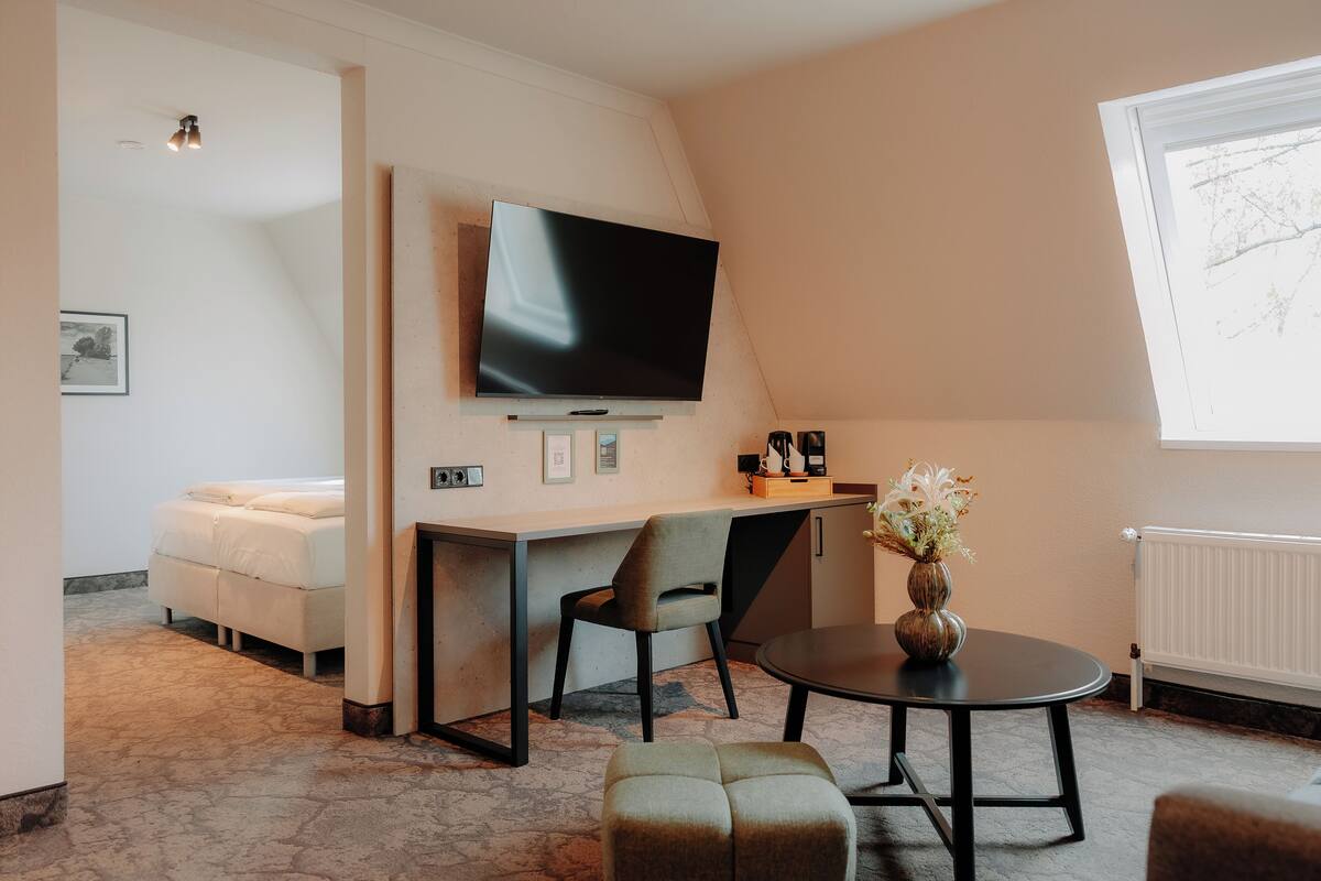 A modern room with a bed, a desk, a chair, a TV, and a vase with flowers.