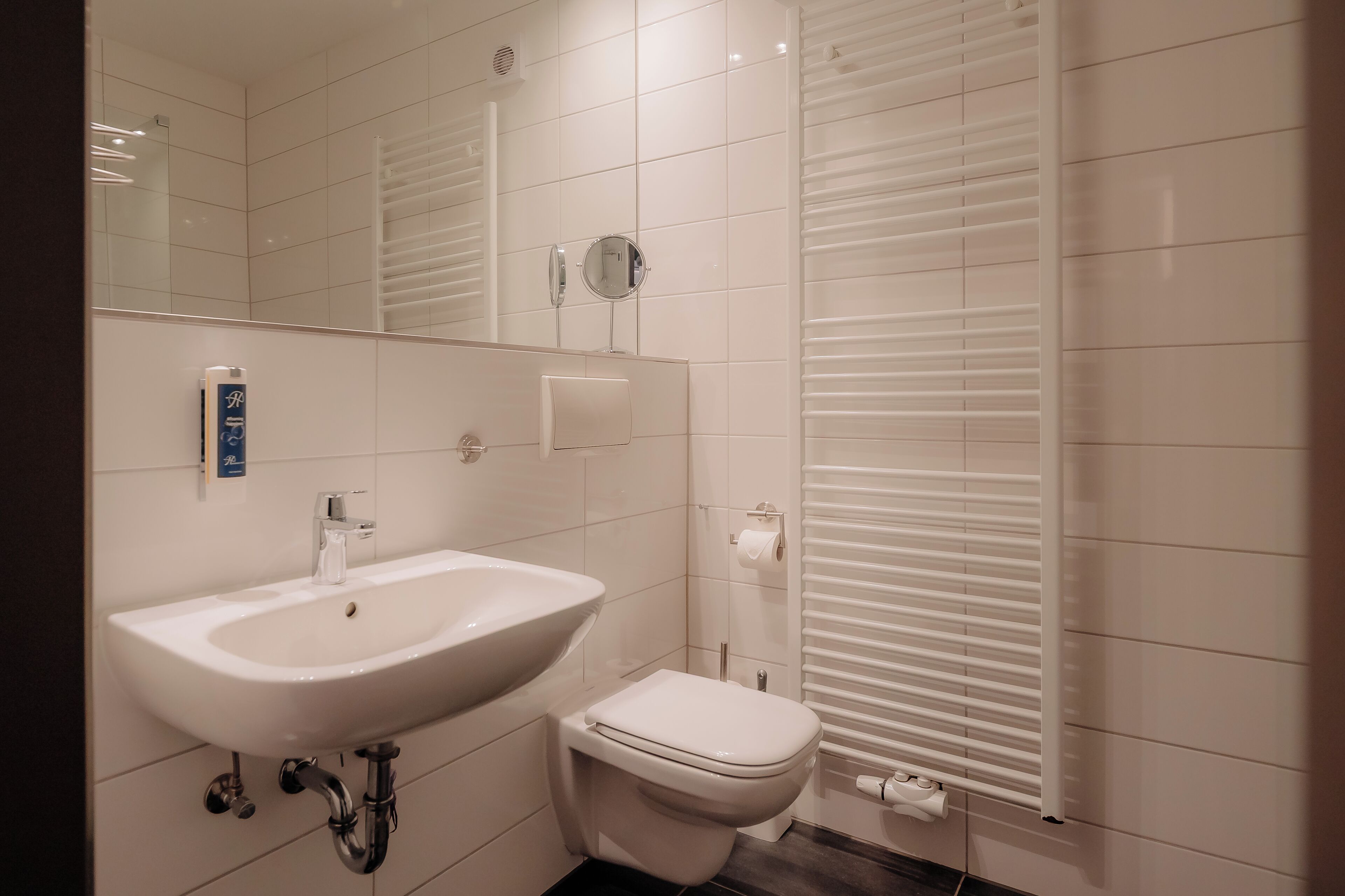Une salle de bain moderne avec un lavabo, des toilettes et un miroir, le tout de couleur blanche.