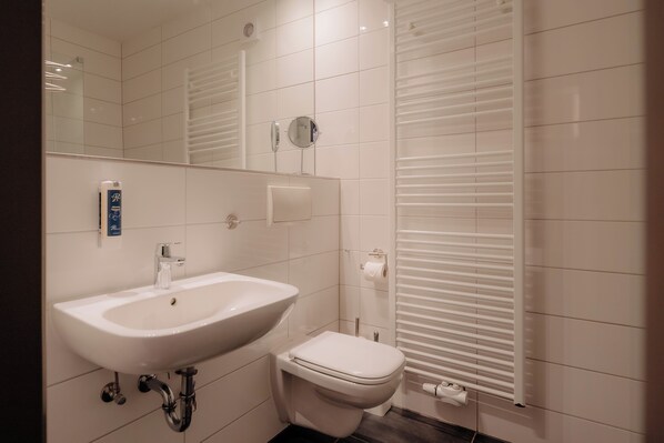 A modern bathroom with a white sink, toilet, and a mirror. - Parkhotel Papenburg by Hackmann (Papenburg)