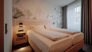 Habitación de hotel con una cama grande, una mesita de noche, una lámpara de pared y un mural floral.