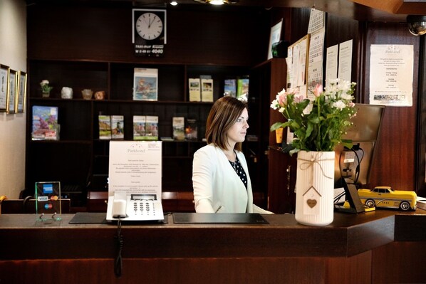 A reception desk with a clock, a phone, and a vase with flowers. - Parkhotel Papenburg by Hackmann (Papenburg)